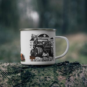 May include: White enamel camping mug featuring a black graphic of a 4x4 off-road vehicle, a campfire, and a person. The mug has a silver rim and a white handle. The mug is sitting on a log.