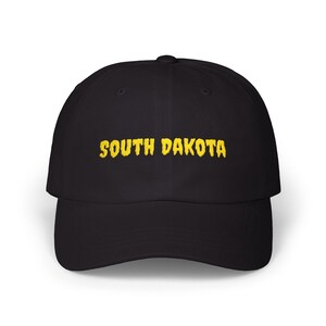 Peut inclure: Casquette de baseball noire avec le texte brodé "SOUTH DAKOTA" en jaune. La casquette a une visière incurvée et une coupe structurée. Un accessoire classique pour un usage décontracté.