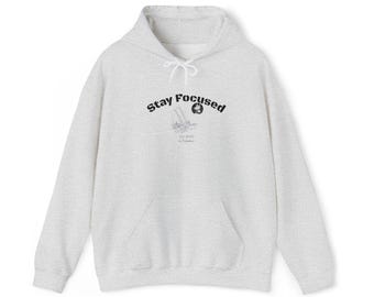 May include: A light grey hoodie with a drawstring hood and a front pocket. The hoodie displays the text "Stay Focused" in black above a small graphic and additional text. The hoodie is made of a soft, comfortable material.