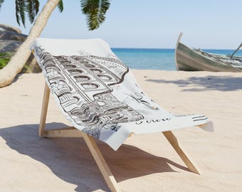 May include: A white beach chair with a black and white architectural illustration on the fabric. The chair is made of light-colored wood and is set on a sandy beach with a boat in the background.