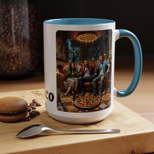 Könnte beinhalten: Weißer Keramikbecher mit türkisfarbenem Innenraum und Henkel. Der Becher zeigt eine farbenfrohe Illustration von drei Personen auf einem Sofa mit Pizza und einem Monster. Das Wort "CO" ist auf der Seite des Bechers aufgedruckt.