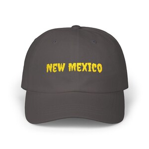 May include: A gray baseball cap with the embroidered text "NEW MEXICO" in yellow. The cap has a curved brim and a classic, unstructured design, suitable for casual wear.