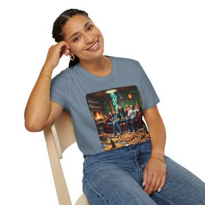 Könnte beinhalten: Hellblaues T-Shirt mit einer farbenfrohen Grafik einer Gruppe von Personen auf einem roten Sofa in einem Raum voller Pizza. Ein grüner Lichtstrahl scheint von der Decke. Das Shirt ist aus weichem Material.