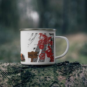 May include: White enamel mug with a silver rim, featuring a red ATV and motorcycle design with tire tracks. The mug has the words "Day Off" on a wooden sign. The mug is sitting on a tree trunk.