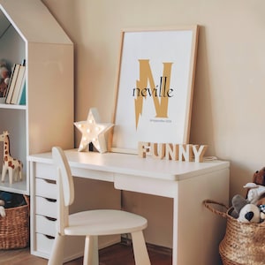 May include: A white desk with a matching chair, a star-shaped light, and a framed print with the name "Neville" in gold. The word "FUNNY" is spelled out in wooden letters. A giraffe toy and a basket are also visible.