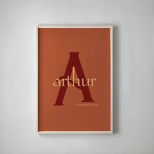 Puede incluir: Impresión artística enmarcada con el nombre "Arthur" en una fuente serif. El nombre se superpone a una gran "A" burdeos sobre un fondo terracota. La fecha "24 de septiembre de 2024" está impresa debajo.