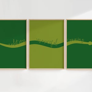Op de afbeelding: Drie ingelijste kunstprints met een groen slangenontwerp. Elke print heeft een andere tint groen als achtergrond. De woorden "ambitieus", "vindingrijk" en "sluw" zijn in een cursief lettertype over elke print geschreven.