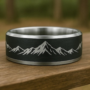 May include: A black and silver ring with a mountain range design engraved on the band.