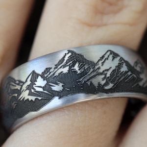 Op de afbeelding: Een zilveren ring met een gegraveerd bergketenontwerp op de band.