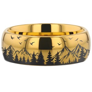 May include: A gold-colored ring with a black mountain and forest design. The ring is a wide band with a rounded top.