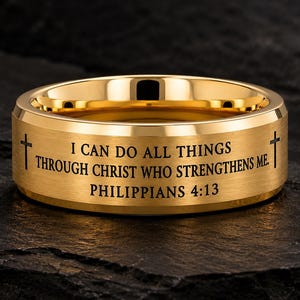 Puede incluir: Un anillo de banda en tono dorado con acabado cepillado, que presenta el texto grabado I CAN DO ALL THINGS THROUGH CHRIST WHO STRENGTHENS ME. PHILIPPIANS 4:13 y un pequeño símbolo de cruz a cada lado de la inscripción en la superficie.