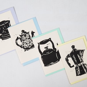 Può includere: Quattro biglietti di auguri con illustrazioni a inchiostro nero di tazze da tè, teiere e una caffettiera. Ogni biglietto ha un bordo di colore diverso: azzurro, verde chiaro e giallo. I biglietti sono su sfondo bianco.