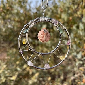 May include: A silver wire circle with a seashell in the center and small colorful stones around the edge.