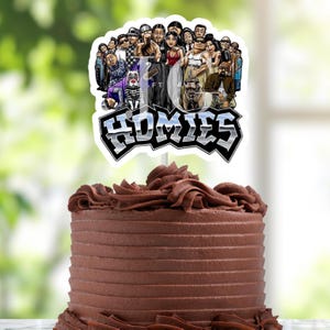 Peut inclure: Un gâteau au chocolat avec une décoration de gâteau représentant un groupe de personnages de dessins animés et le mot "HOMIES" dans un design argenté et noir. Le gâteau a une surface lisse et striée et est garni de glaçage au chocolat.