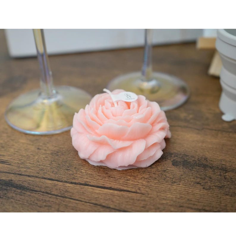 May include: A pink flower-shaped candle with a white label that says "Soy Candle".