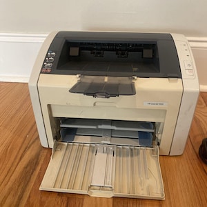 May include: A white HP LaserJet 1022 printer with the paper tray open. The printer has a black front panel with buttons and a small LCD screen.