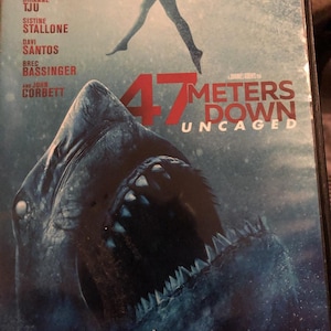 May include: DVD case for the movie "47 Meters Down: Uncaged." The cover features a large shark with open jaws, a woman's silhouette, and the tagline "Fear Runs Deep." Cast names are listed at the top.