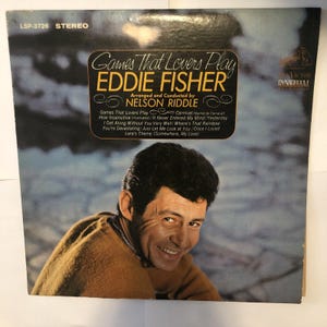 Könnte beinhalten: Vintage Vinyl-Schallplattenhülle für "Games That Lovers Play" von Eddie Fisher. Das Cover zeigt ein Porträt von Eddie Fisher und den Albumtitel in goldener Schrift. Das Album enthält von Nelson Riddle arrangierte Songs.