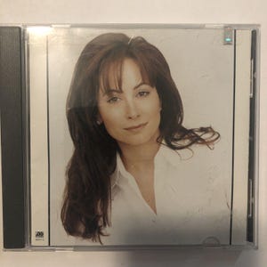 May include: A CD case featuring a woman with long, dark brown hair and a white collared shirt. The woman is looking at the viewer with a slight smile. The CD case has a black spine and the Atlantic Records logo.
