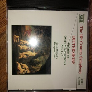 May include: A CD case for Dittersdorf's "The 18th Century Symphony". The cover art shows a classical painting of nude figures. The CD case is in a black plastic case.