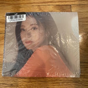 Könnte beinhalten: Eine Nahaufnahme eines Frauen Gesichts mit langen, dunklen Haaren. Sie trägt ein pfirsichfarbenes Shirt und blickt nach links. Das Bild ist leicht verschwommen und hat eine weiche, verträumte Atmosphäre.