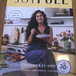 May include: A cookbook titled "Joyfull" with a yellow cover featuring a woman holding a bowl of food. The book cover also includes the text "More than 125 Plant-Based Recipes" and "Cook Effortlessly, Eat Freely, Live Radhi." A Target logo with a 30% off discount is in the bottom right corner.