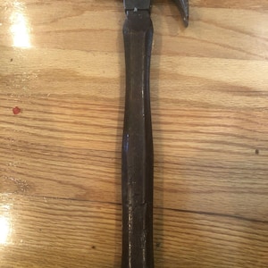 Op de afbeelding: Een vintage hamer met een houten steel en een metalen kop. De hamer heeft een licht gebogen klauw en een versleten houten steel.