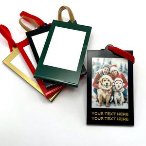 May include: A collection of rectangular hanging ornaments with colored frames in green, black, red, and gold. Each ornament features a white center panel for customization and a velvet ribbon loop. One black ornament displays a photo of two people and two dogs.
