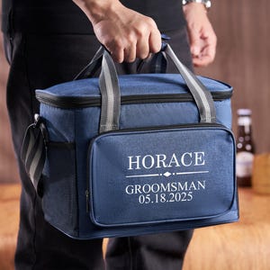 Puede incluir: Una bolsa de enfriador azul aislada con una cremallera negra y un dise&ntilde;o bordado blanco que dice "HORACE GROOMSMAN 05.18.2025".