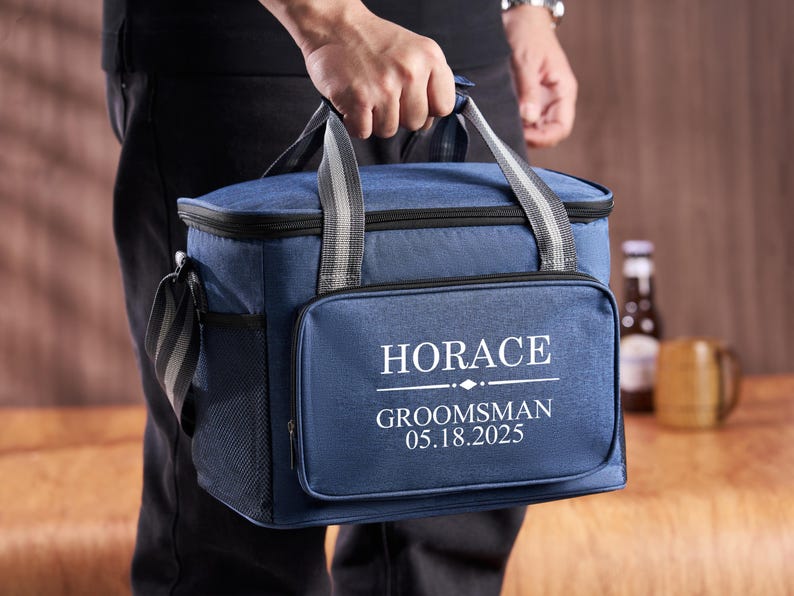 Puede incluir: Una bolsa de enfriador azul aislada con una cremallera negra y un dise&ntilde;o bordado blanco que dice "HORACE GROOMSMAN 05.18.2025".