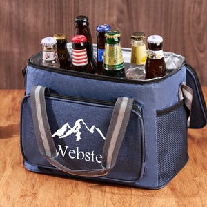 Puede incluir: Una bolsa de enfriador aislada azul con un dise&ntilde;o de monta&ntilde;a blanca y la palabra "Webste" impresa en la parte delantera. La bolsa tiene una parte superior con cremallera y dos asas. La bolsa est&aacute; llena de varias botellas de cerveza.