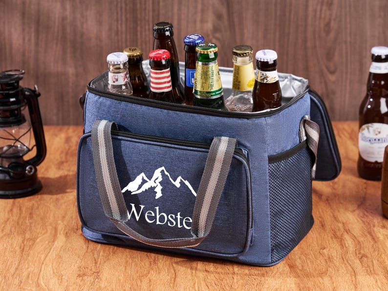 Puede incluir: Una bolsa de enfriador aislada azul con un dise&ntilde;o de monta&ntilde;a blanca y la palabra "Webste" impresa en la parte delantera. La bolsa tiene una parte superior con cremallera y dos asas. La bolsa est&aacute; llena de varias botellas de cerveza.