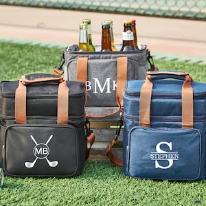 May include: Three insulated cooler bags with brown leather handles. The bags are gray, black, and blue. The gray bag has the initials "BMK" embroidered on it. The black bag has a golf club design and the initials "MB". The blue bag has the name "STEPHEN" embroidered on it.