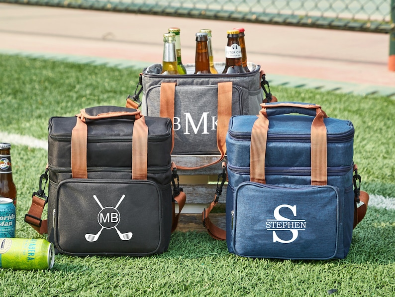 May include: Three insulated cooler bags with brown leather handles. The bags are gray, black, and blue. The gray bag has the initials "BMK" embroidered on it. The black bag has a golf club design and the initials "MB". The blue bag has the name "STEPHEN" embroidered on it.