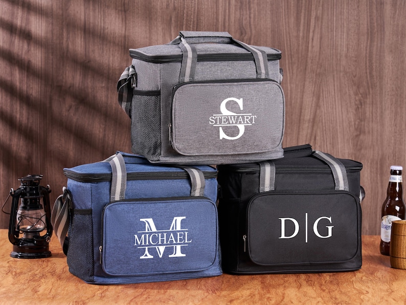 Puede incluir: Tres bolsas isot&eacute;rmicas personalizadas. La primera bolsa es gris con el nombre "Stewart" y la inicial "S" en blanco. La segunda bolsa es azul con el nombre "Michael" y la inicial "M" en blanco. La tercera bolsa es negra con las iniciales "D|G" en blanco.