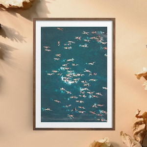 May include: Framed aerial photograph of a group of people swimming in teal water. The swimmers are scattered throughout the frame, with some appearing to be wearing swim caps. The photograph is in a brown wooden frame.