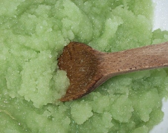 Puede incluir: Primer plano de una sustancia granular verde claro, posiblemente un exfoliante o pasta, que se agita con una cuchara de madera. La textura parece áspera y ligeramente húmeda, con un color brillante y fresco.