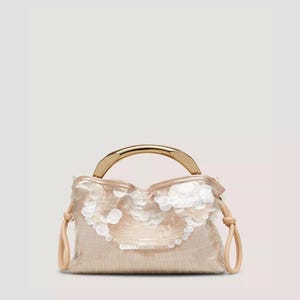 Puede incluir: Un pequeño bolso beige con un asa dorada. El bolso está adornado con lentejuelas blancas y tiene correas beige de imitación de cuero. El diseño del bolso es elegante y adecuado para ocasiones especiales.