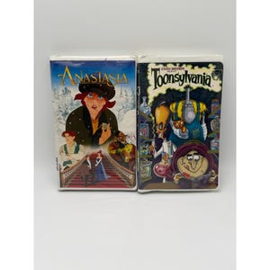 Könnte beinhalten: Zwei VHS-Kassetten nebeneinander. Die linke Kassette zeigt den Animationsfilm Anastasia mit Charakteren auf einer Treppe vor einer verschneiten Kulisse. Die rechte Kassette zeigt Steven Spielberg Presents Toonsylvania mit Zeichentrickfiguren.