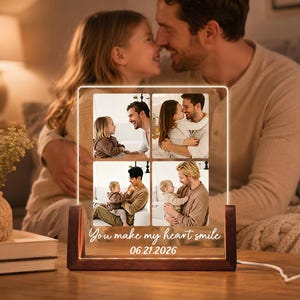 May include: A personalized photo display with four family photos, illuminated by a warm light. The wooden base supports a clear acrylic panel with the text "You make my heart smile" and the date 06.21.2026.