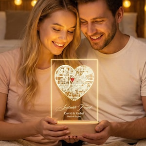 May include: A heart-shaped map light with a wooden base. The map is etched into a clear acrylic panel and illuminated with a warm glow. The text "Soulmate Found" and names are visible. The light is held by a couple.