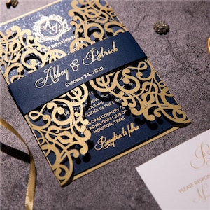 Peut inclure: Un faire-part de mariage bleu marine avec des panneaux en filigrane doré découpés au laser. Une bande ventrale bleu marine affiche les noms Abbey & Patrick et la date du 24 octobre 2020 en écriture dorée. Le texte mentionne le Royal Oaks Country Club.