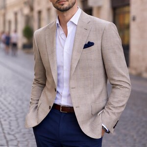 Può includere: Una giacca beige a quadri, camicia bianca e pantaloni blu navy. La giacca ha un fazzoletto da taschino e una cintura in pelle marrone. Un completo classico ed elegante.