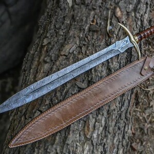 May include: A sword with a brown leather scabbard. The sword has a silver blade with a decorative pattern and a gold handle. The scabbard has a brown leather strap.