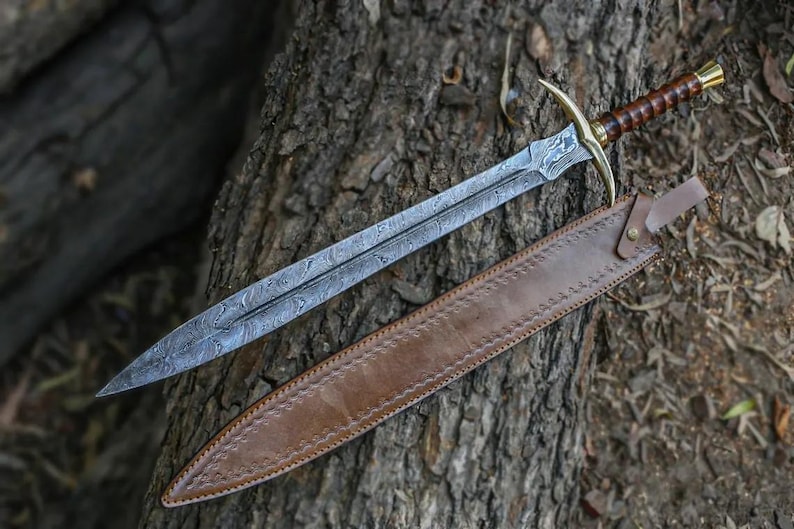 May include: A sword with a brown leather scabbard. The sword has a silver blade with a decorative pattern and a gold handle. The scabbard has a brown leather strap.