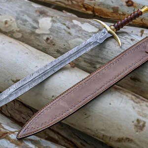 May include: A sword with a brown leather scabbard and a damascus steel blade. The sword has a gold-colored hilt and a brown wooden handle.