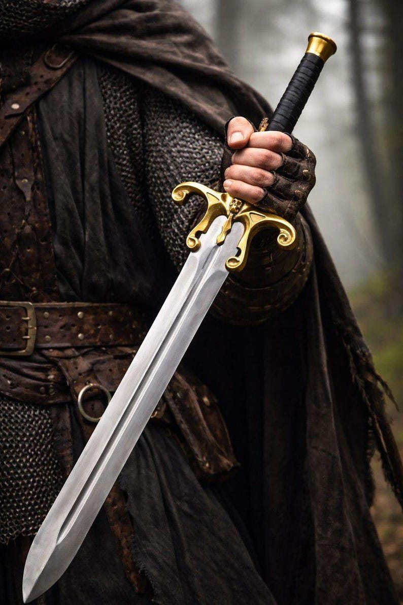 May include: A silver sword with a gold hilt and black handle is held in a gloved hand. The sword has a double-edged blade and ornate gold detailing. The person is wearing a dark cloak and leather armor.