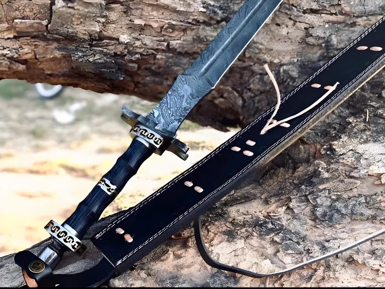 May include: A black leather scabbard with a decorative stitch pattern and a black and silver sword with a wooden handle. The sword has a Damascus steel blade with a decorative pattern.