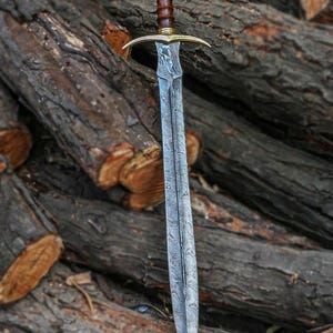 May include: A long, silver sword with a wooden handle and a gold pommel. The sword is lying on a pile of logs.