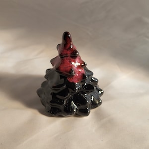 May include: A small ceramic Christmas tree ornament with a black base and a red and black top.
